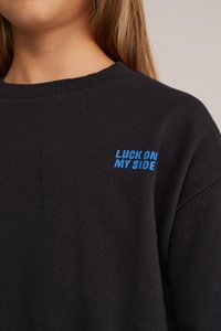 Pulover negru cu guler rib captusit, avand pe față text brodat albastru "LUCK ON MY SIDE". Textură moale, design casual.