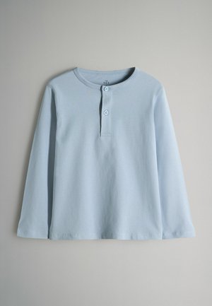 Chemise à manches longues bleu clair en tissu doux, dotée d'un col henley avec deux boutons et d'un ourlet droit. Design minimal, sans motifs.