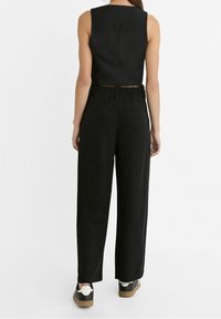 Zwarte mouwloze top gecombineerd met losse zwarte broek. De broek heeft een hoge tailleband, achterzakken en een ontspannen fit. Geaccentueerd met sneakers.