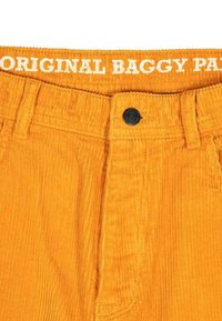 Manžetové nohavice v jasne oranžovej farbe s ryhovanou textúrou, s čiernym gombíkom a nápisom "ORIGINAL BAGGY PANTS" potlačeným na páse.