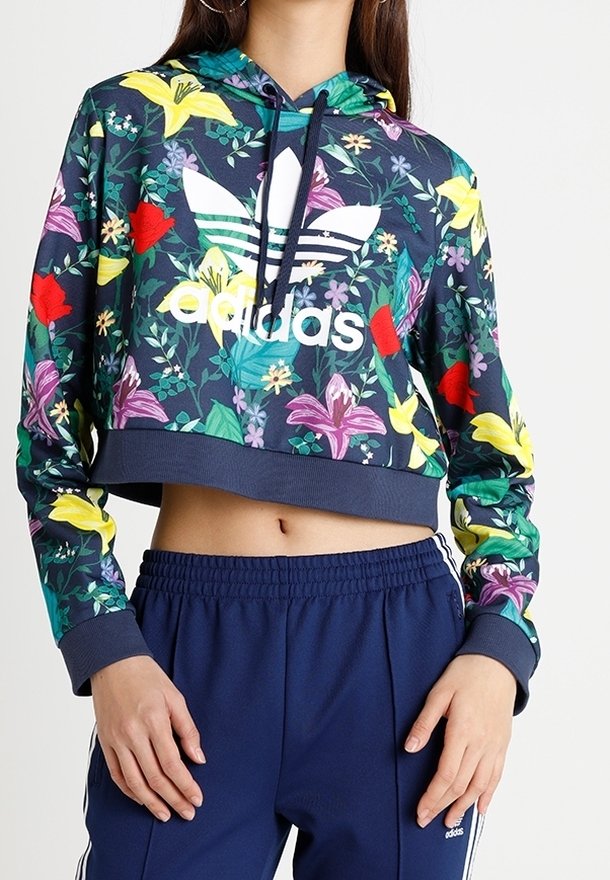 Felpa corta blu navy con motivo floreale e grande logo Adidas bianco, dotata di cappuccio con stringhe e polsini a coste. Abbinata a pantaloni blu navy.