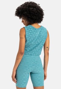 A teal activewear set featuring textured fabric with a repeating floral pattern. The sleeveless top pairs with mid-thigh shorts.