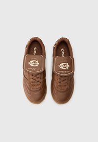 Bruine leren Coach sneakers met veters en een grote gemarkeerde flap over de tong, met lederen vlekkenaccenten aan de binnenkant van de kraag.