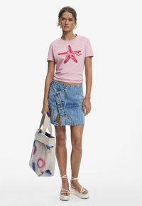 Pink cotton t-shirt with a starfish design, paired with a blue denim wrap skirt. Model holds a canvas tote bag with colorful circular patterns.