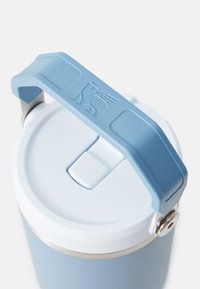 Contenedor aislado con un mango de silicona azul claro, tapa blanca y cuerpo de acero inoxidable. Presenta un logotipo en el mango y un cierre seguro.