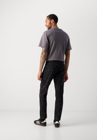 Grey cotton t-shirt with a crew neckline, paired with black marble-patterned jeans. Worn with black sneakers featuring white stripes.
