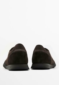 Scarpe in suede marrone scuro con profilo basso, finitura texture e suole in gomma nera. Presentano una cucitura sottile e un design del tacco arrotondato.