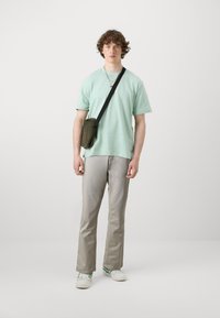 Piparmētru zaļš īsām piedurknēm t-krekls, pelēkas taisna piegriezuma bikses, baltas kedas ar zaļiem akcentiem un mazs olīvu krāsas plecu soma.