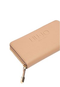 Portafoglio beige con zip, superficie testurizzata, logo impresso e dettagli in oro. Presenta un tirazip decorativo.