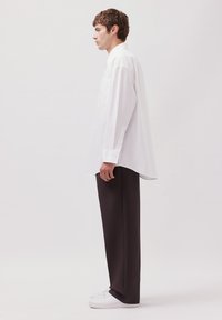 Camicia bianca oversize con bottoni e maniche lunghe, con taschino sul petto, abbinata a pantaloni scuri larghi e sneakers bianche.