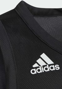 Top atlético negro sin mangas con una tela texturizada y detalles de malla, que presenta un prominente logo blanco de Adidas en el frente.