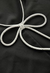 Svart tyg med en silverfärgad rhinestone-båge i mitten. Slät textur med kontrasterande glänsande accenter runt bågen.