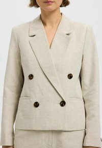 Beige dobbeltknappet blazer lavet af linned, med store mørkebrune knapper, en notch-krave og to forlommer.