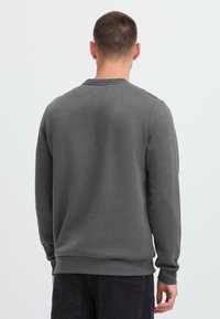 Felpa grigia con maniche lunghe, colletto a girocollo e polsini a coste. Realizzata in tessuto morbido, con una texture liscia e un design minimale.