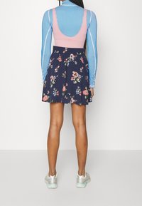 Top senza maniche rosa abbinato a una gonna floreale blu navy. La gonna presenta un design stampato e l'outfit è completato da sneakers argento e turchesi.