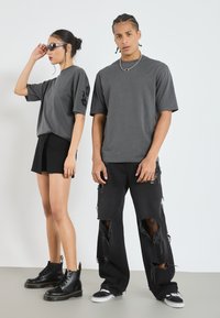 Grå oversized t-shirts på två modeller, kombinerade med svarta shorts och rivna svarta jeans. Svarta kängor och sneakers fulländar outfiten.