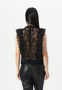 Haut sans manches en dentelle noire avec des bords festonnés, des motifs floraux complexes et un dos transparent ; associé à un pantalon en cuir noir ajusté.