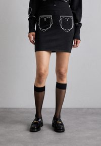 Fustă din tricot negru cu buzunare în formă de inimă conturate cu cusături albe, asortată cu șosete negre până la genunchi și mocasini negri lucioși.