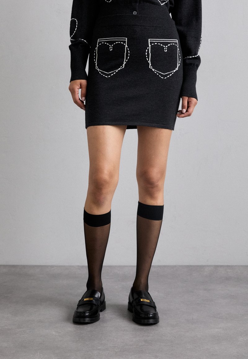 Fustă din tricot negru cu buzunare în formă de inimă conturate cu cusături albe, asortată cu șosete negre până la genunchi și mocasini negri lucioși.