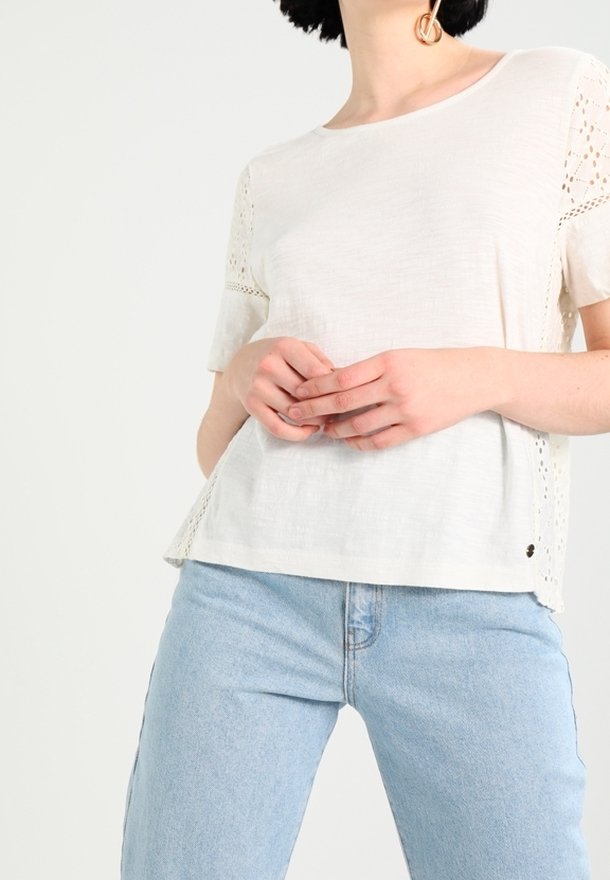 Wit linnen T-shirt met korte mouwen en kantdetails. Gecombineerd met lichtblauwe spijkerbroek. Eenvoudige snit en comfortabele pasvorm.