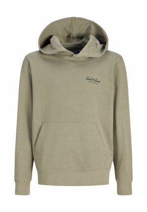 Enfant aux cheveux blonds courts portant un sweat à capuche vert clair, un jean bleu large et des chaussures beiges, debout et regardant vers la droite.