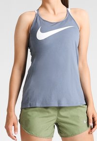 Szary sportowy podkoszulek z białym logo Nike w kształcie łuku, w zestawie z zielonymi szortami o subtelnym połysku i małym logo łuku.