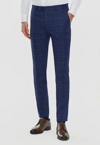Granatowe w kratę spodnie w kant o dopasowanym kroju, z płaskim przodem, kieszeniami bocznymi, w zestawie z brązowymi skórzanymi butami.