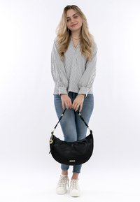 Borsa in pelle nera con una forma curva e una superficie texturizzata, dotata di una tracolla intrecciata e di un accento metallico. Indossata con jeans casual e sneakers.
