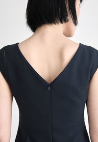 Black sleeveless dress with a V-neck back, featuring a subtle zipper closure. Smooth fabric with a tailored fit and minimal design.