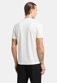 T-shirt bianco a maniche corte con un design pulito e aderente. Tessuto liscio, scollatura rotonda e dettagli di cucitura delicati lungo le maniche e l'orlo.
