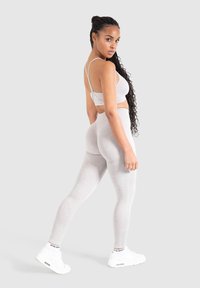 Set di reggiseno sportivo e leggings grigi chiaro, realizzato in un materiale morbido e elasticizzato, con spalline sottili e una texture liscia. Sneakers bianche completano l'outfit.