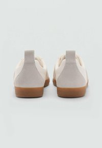 Sneaker bianca e grigia chiara con un tallone in suede, suola in gomma naturale e design minimalista, dotata di una linguetta sul retro.
