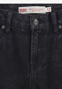 Vaqueros de mezclilla negra con corte recto, con bragueta de botones, cinco bolsillos y una etiqueta que dice "Levi's 551Z Authentic Straight", talla 12.