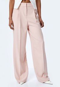 Lichtroze wijde pantalons met een gladde textuur, met voorplooien en een hoge taille, gecombineerd met puntige witte hakken.
