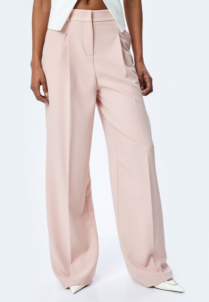 Lichtroze wijde pantalons met een gladde textuur, met voorplooien en een hoge taille, gecombineerd met puntige witte hakken.