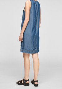 Denim šaty bez rukávů s volným střihem, délka do poloviny stehna, s rovnými švy na zádech a jemnými detaily prošívání. Černé sandály na tenkých řemíncích.