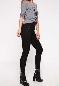 Grå långärmad tröja med grafisk design, kombinerad med svarta slim-fit byxor med sidoknappar. Modell bär svarta klackstövlar.