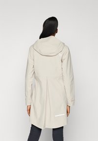 Beige vattentät jacka med huva, två sidofickor och reflekterande detaljer. Har en plisserad rygg och långa ärmar.