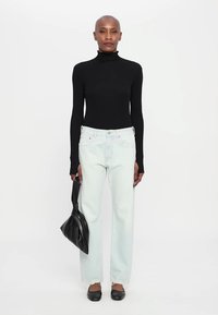 Top de cuello alto negro de manga larga combinado con jeans de pierna recta de color azul claro, zapatos planos negros y un bolso estructurado negro.