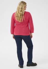 Pull en laine rose avec un motif texturé, col rond et manches longues. Associé à un jean bleu foncé et des chaussures à plateforme noires.