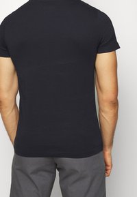 Tummansininen puuvillainen t-paita lyhyillä hihoilla, slim-fit-malli ja sileä pinta. Sisältää pyöreän kaula-aukon ja hieman kaarevan helman.