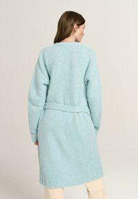 Light blue knitted cardigan with long sleeves, a belt at the waist, and ribbed hem details. Soft texture and loose fit.