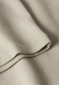 Helle beige gerippte Stoff mit einem subtilen Glanz, der eine weiche Textur und glatte Kanten aufweist. Der Stoff ist gefaltet und zeigt Tiefe und Dimension.