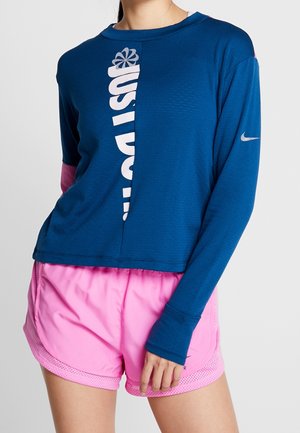 Blauwe lange mouw top met "JUST DO IT" logo en roze accenten, gecombineerd met roze sportshorts met mesh-details en elastische tailleband.