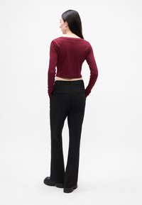 Top lung cu maneci lungi de culoare marsala, scurt, asortat cu pantaloni negri evazați. Pantalonii au buzunare la spate și o textură de țesătură netedă.