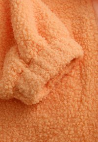 Tela de forro polar suave en naranja claro con una textura rizada, mostrando un primer plano de un puño recogido o detalle de manga.