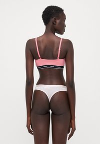 Soutien-gorge rose avec bande logo noire et bretelles réglables, associé à un string blanc avec une taille de marque, en tissu lisse et offrant une couverture minimale.
