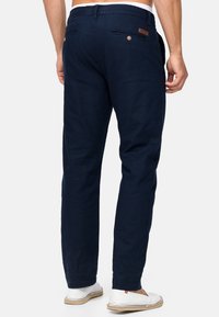 Pantaloni in lino blu navy con dettaglio a bottone sulla tasca posteriore. Vestibilità rilassata con una trama morbida e cintura elastica. Calzature casual.