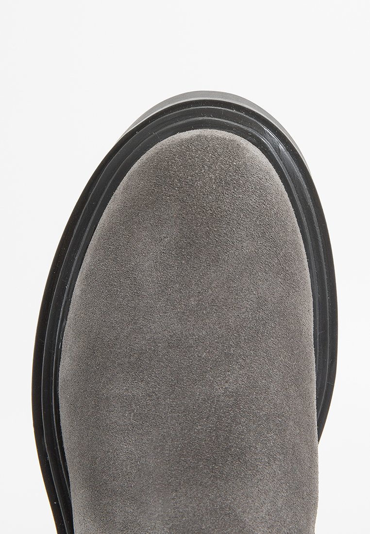 Stivaletto grigio in suede con punta rotonda, suola in gomma nera e dettagli di cucitura minimi, caratterizzato da una texture liscia e una leggera lucentezza.