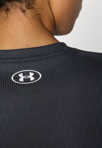 Sort ribbet stof med rund halsudskæring, der har et lille hvidt Under Armour-logo i nakken.
